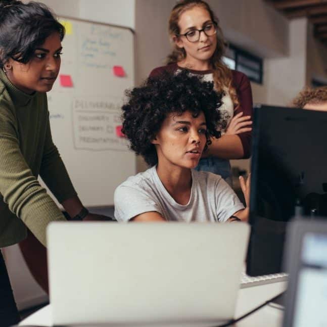 Software engineers working on project together Software engineers working on project and programming in company. Startup business group working as team to find solution to problem. Woman programmer working on computer with colleagues standing by.
